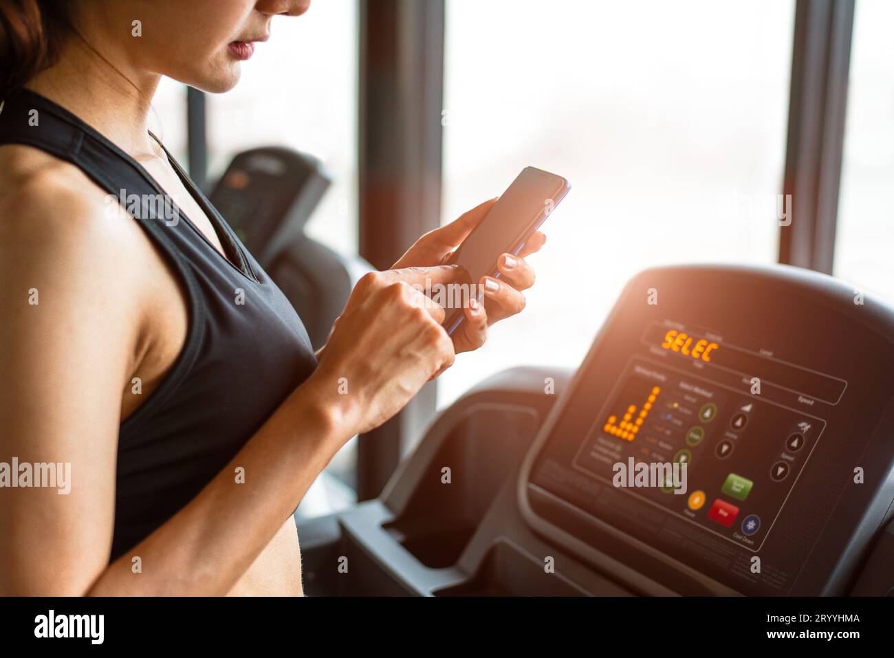 Frau, die ihr Smartphone beim Workout oder Krafttraining im Fitnessstudio auf dem Laufband benutzt. Relax- und Technologiekonzept. Sport Exer Stockfoto