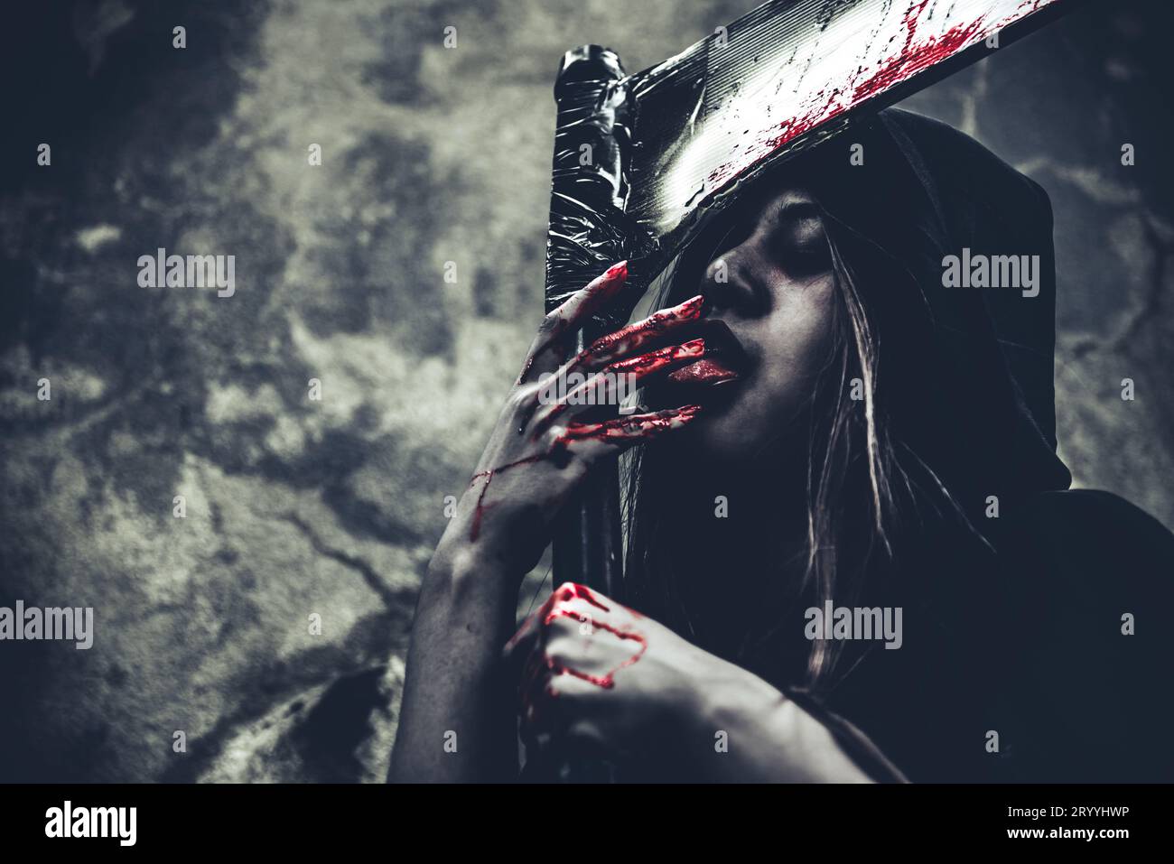 Hexe leckt Blut an den Fingern. Weiblicher Dämonenenengel in schwarzer Kleidung und Kapuze auf Grunge-Wand-Hintergrund. Halloween-Tag und Myster Stockfoto