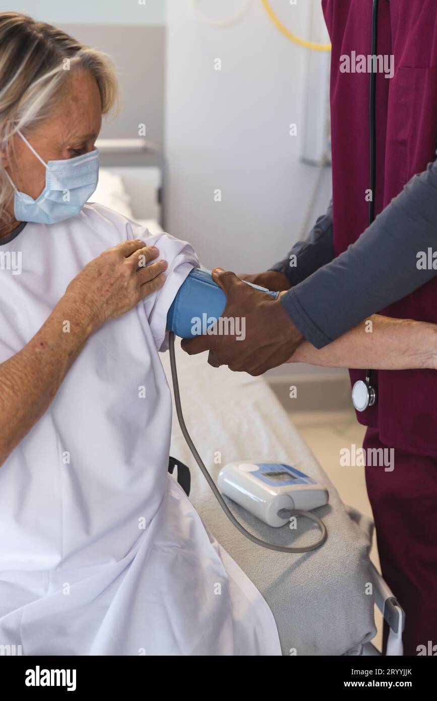 afroamerikanischer Arzt, der den Blutdruck des älteren Kaukasier-Patienten misst, der Gesichtsmasken trägt Stockfoto