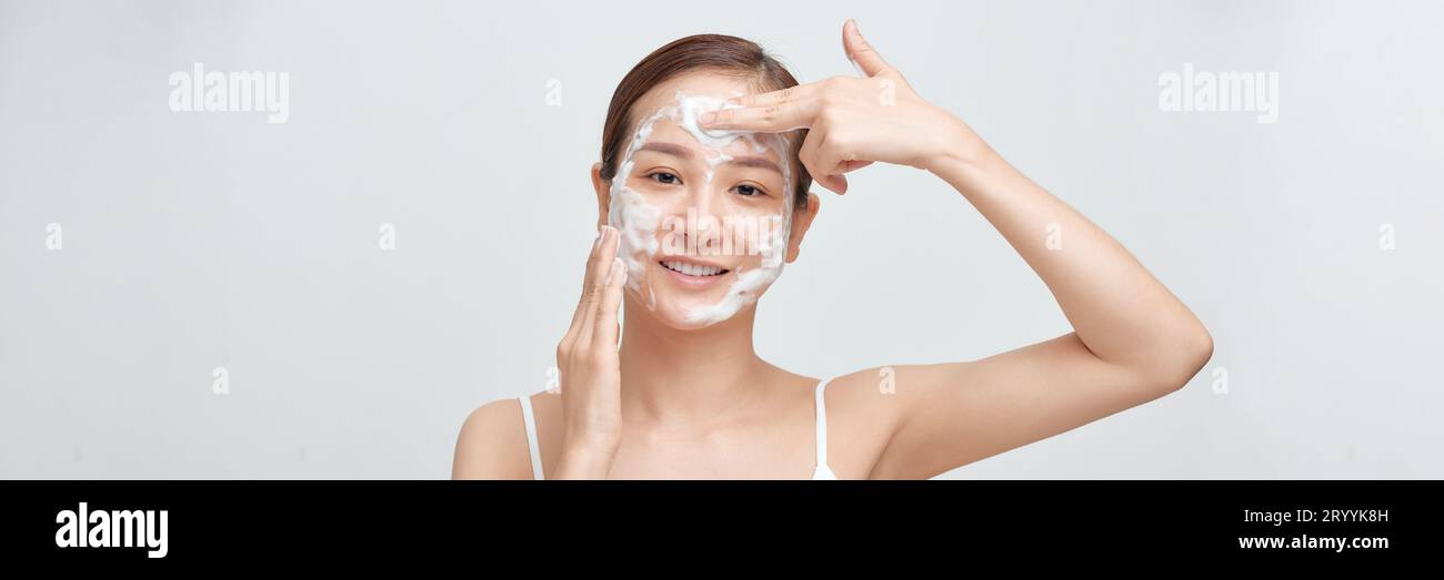 Erntegutfröhliche junge Frau lächelt beim Säubern des Gesichts mit Schaum während der Hautpflege. Panorama Stockfoto