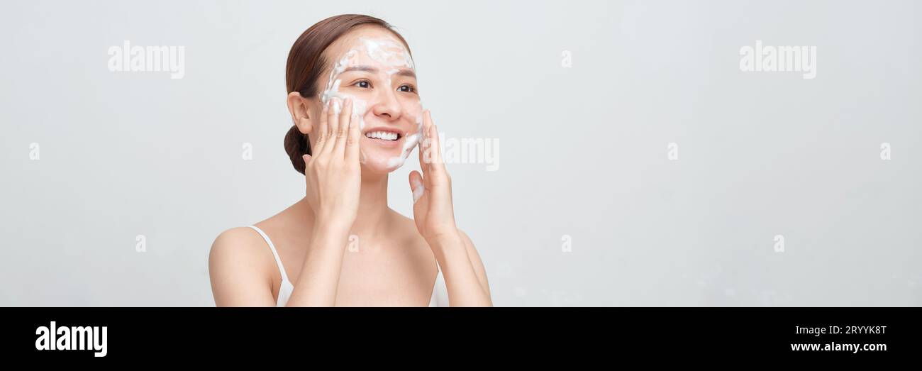 Glückliche Frau mit schäumendem Gesichtsreiniger waschendem Gesicht isoliert auf weißem Banner Hintergrund. Stockfoto