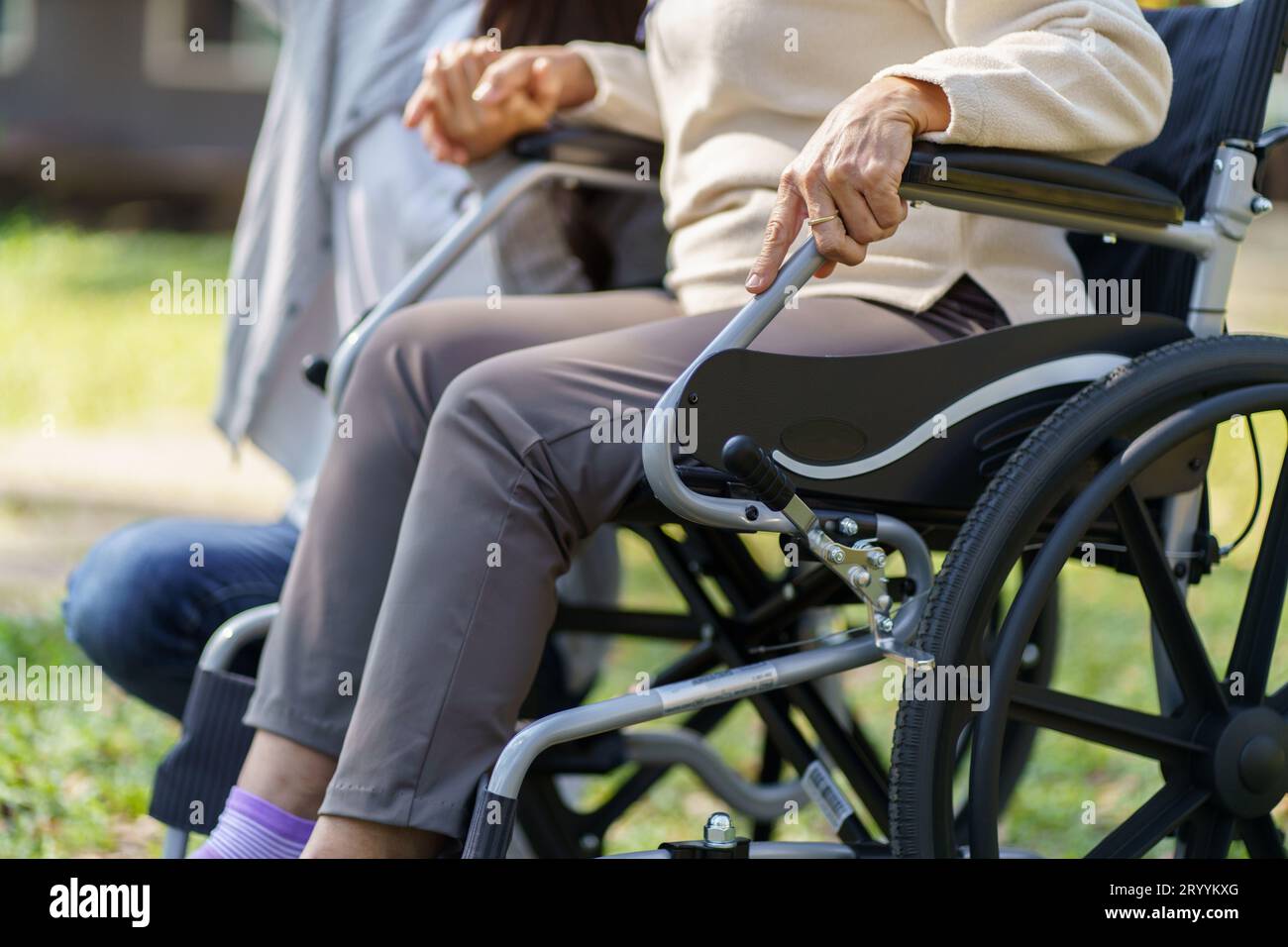 Familienbeziehung Asiatische Seniorin im Rollstuhl mit glücklicher Tochter, die eine Pflegeperson um die Hand hält, während sie Zeit mit dem Kind verbringt Stockfoto