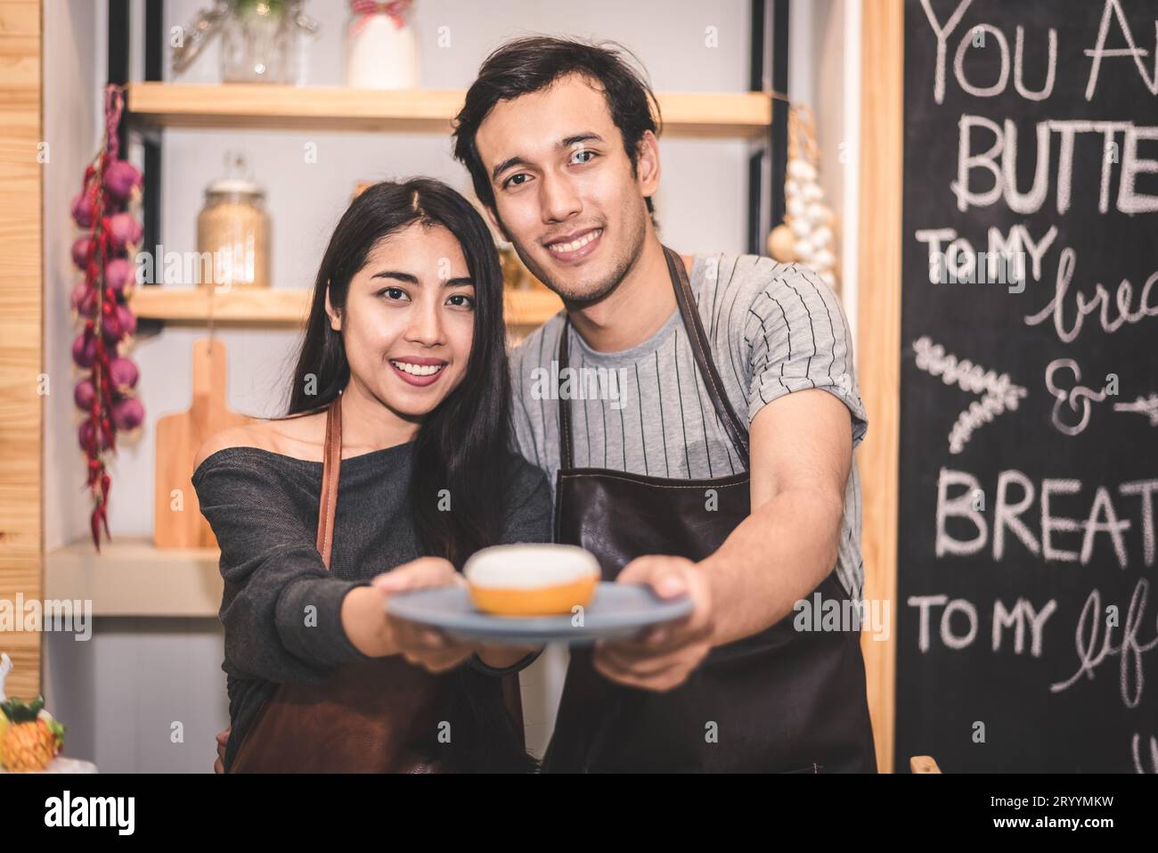 Junge Paare, die als Unternehmer Donuts und Brot in der Bäckerei herstellen. Mann und Frau kochen zusammen Stockfoto
