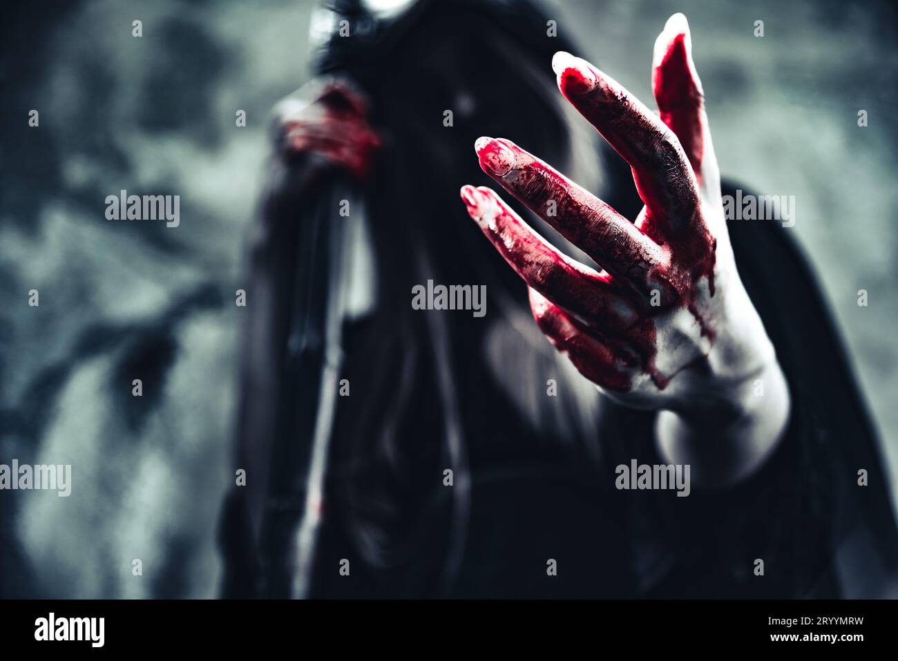 Hexe zeigt blutige Hand. Weiblicher Dämonenenengel in schwarzer Kleidung und Kapuze auf Grunge-Wand-Hintergrund. Halloween-Tag und Mystery Concept Stockfoto