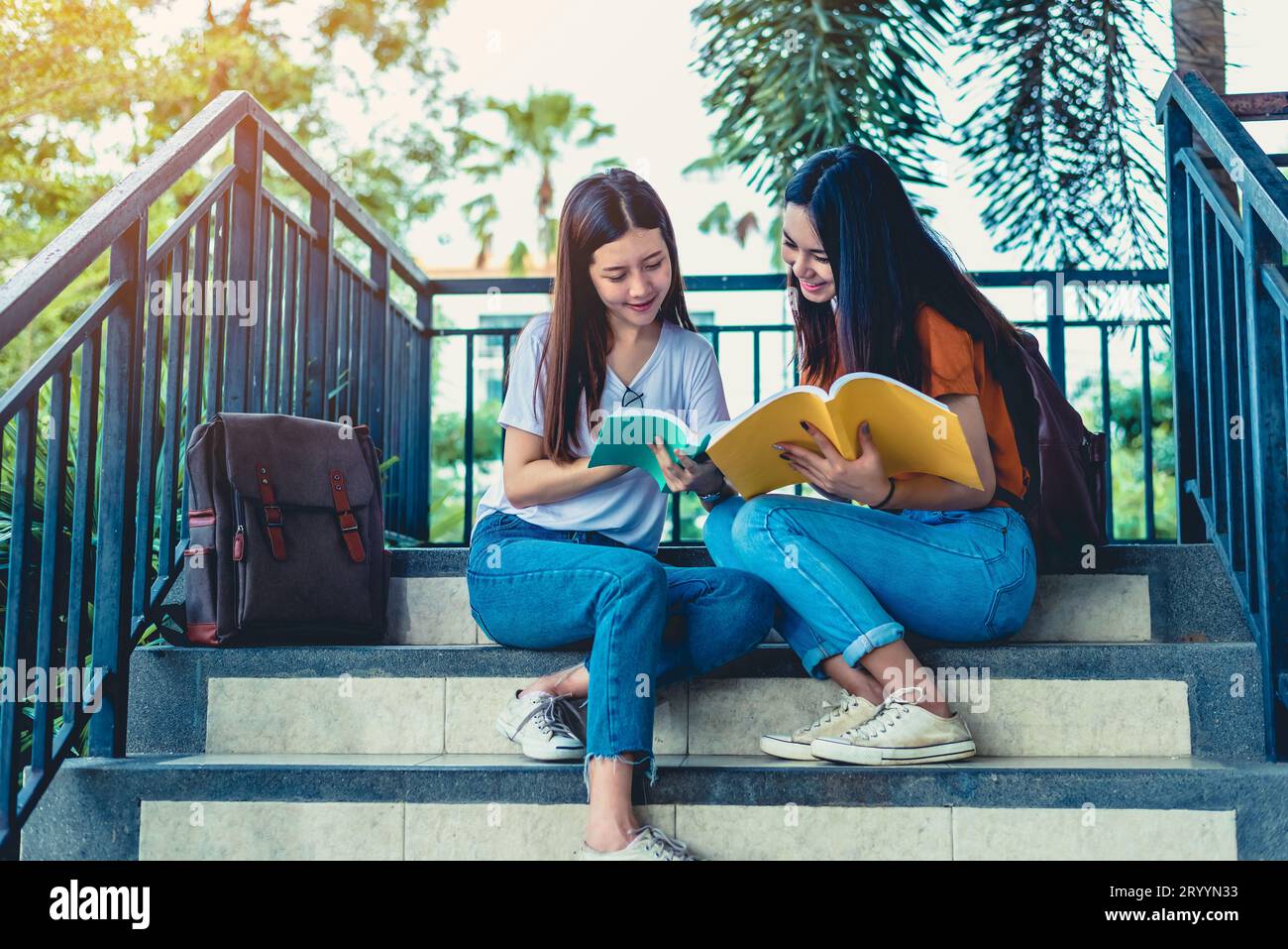 Zwei asiatische Schönheitsmädchen, die Bücher für die Abschlussprüfung lesen und unterrichten. Der Schüler lächelt und sitzt auf der Treppe. Bildungswesen Stockfoto