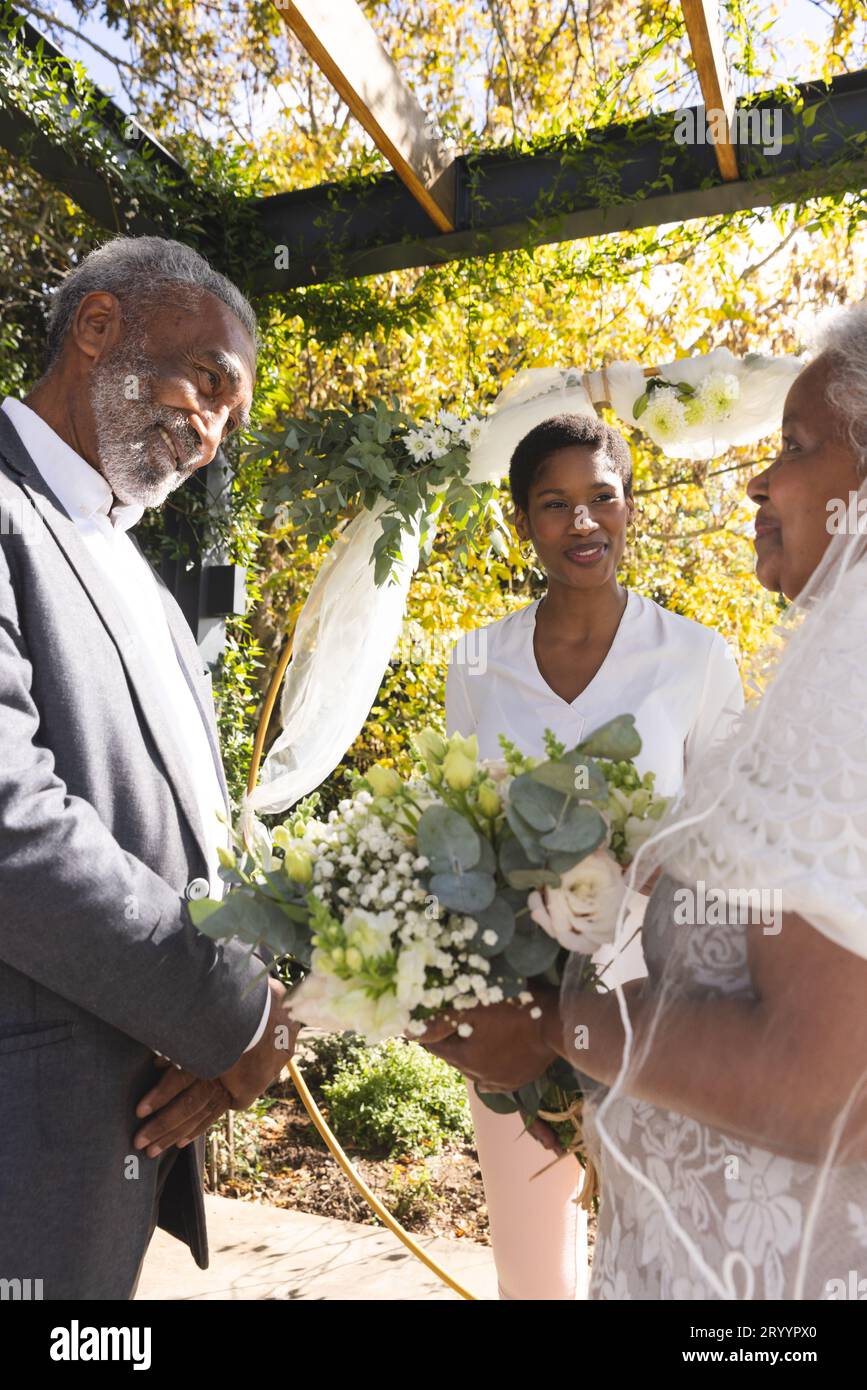 Glückliche, birassistische Frau, Ehefrau mit älterem Paar während der Hochzeit im sonnigen Garten Stockfoto