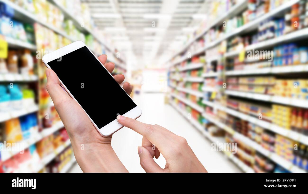 Frau hält Smartphone und Touch Button von Hand mit leerem Bildschirm für Werbung, verschwommenem Supermarkt Hintergrund, Technologie A Stockfoto