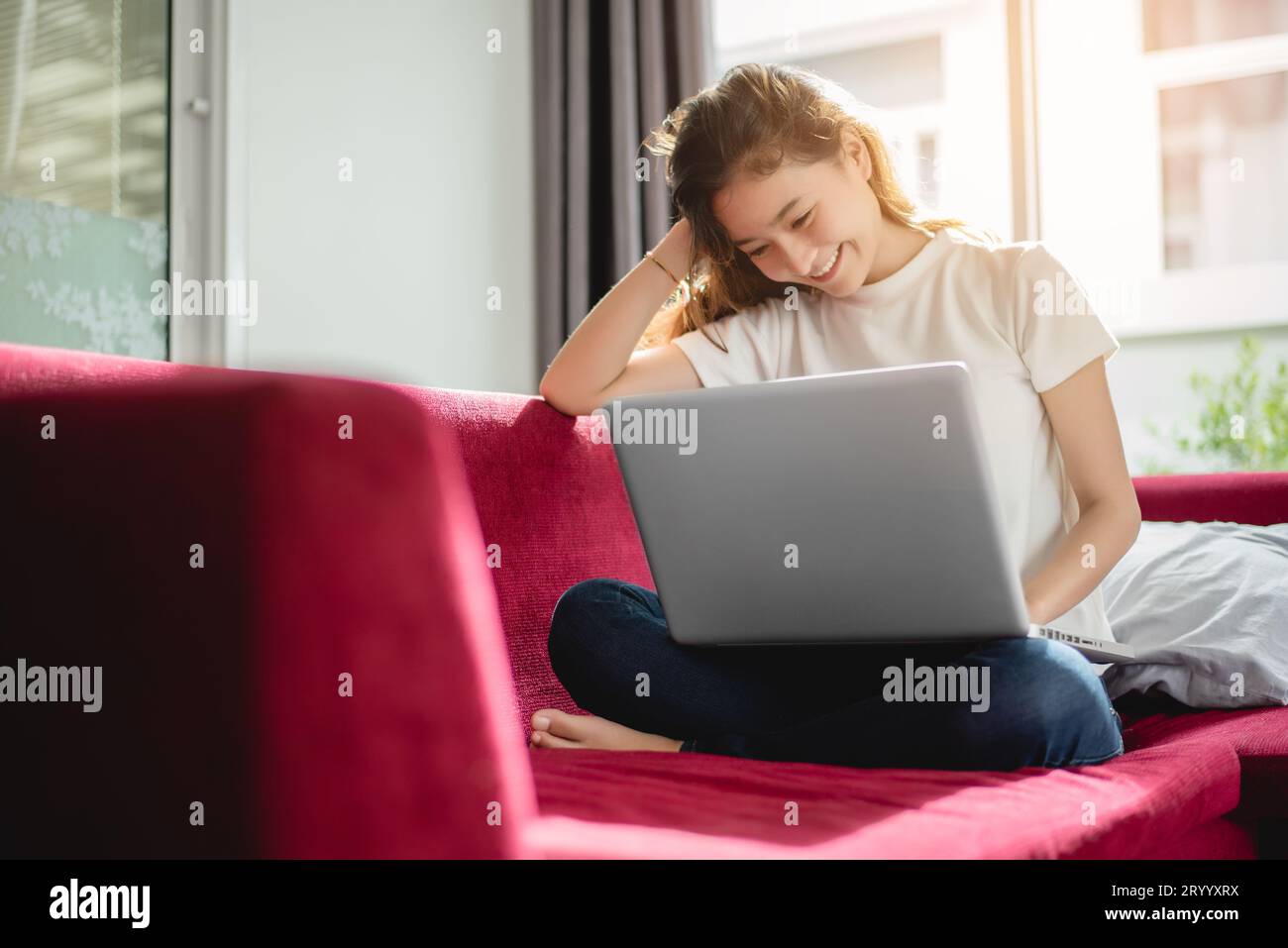 Junge Frau Einkaufen online mit Internet in fröhliche Stimmung auf dem roten Sofa. Business- und Arbeitskonzept, Entspannen und Konzept Stockfoto