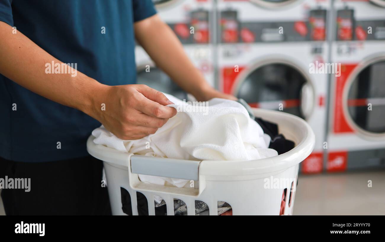 Hausmann mit Korb und schmutziger laundryÂ gewaschener Kleidung im Waschraum. Waschen machineÂ im Wäschereigeschäft Stockfoto