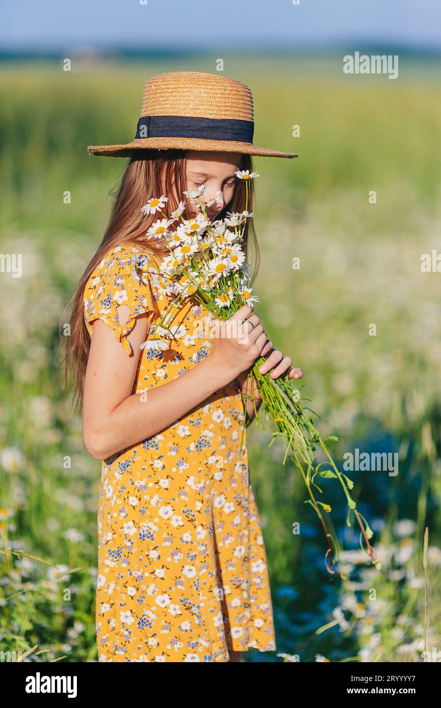 Porträt eines Mädchens in gelbem Kleid und Strohhut auf einem Kamillenfeld im Sommer Stockfoto