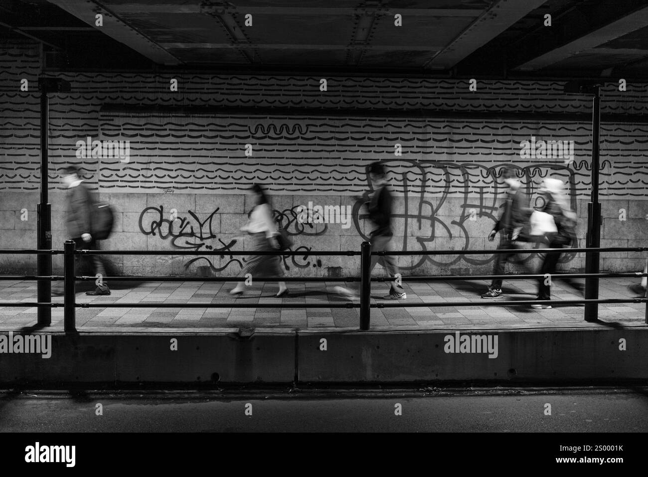 Tokios Unterführung in Schwarz-weiß zeigt das flüchtige Tempo der Pendler, städtische Graffitis und den zeitlosen Rhythmus des Stadtlebens. Stockfoto
