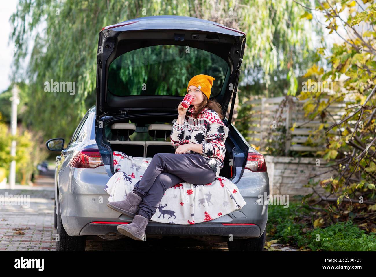 Frau in gelber Mütze, die mit Kaffee im Kofferraum sitzt Stockfoto