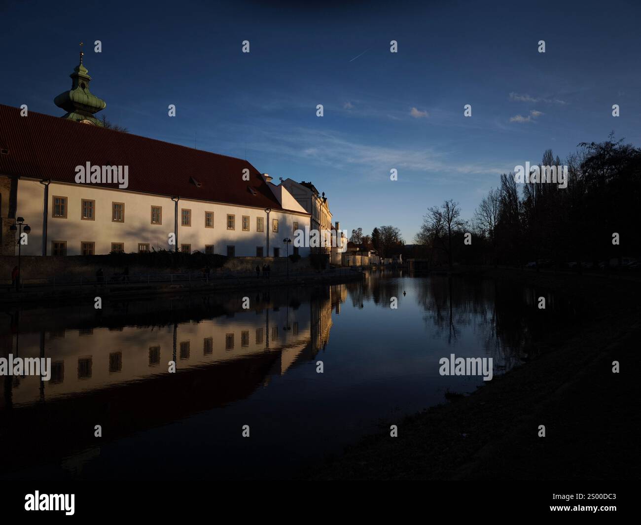 Ceske budejovice, Tschechische republik - 21. Dezember 2024: Dominikanerkloster reflektiert in der Abenddämmerung auf dem Malse-Fluss Stockfoto