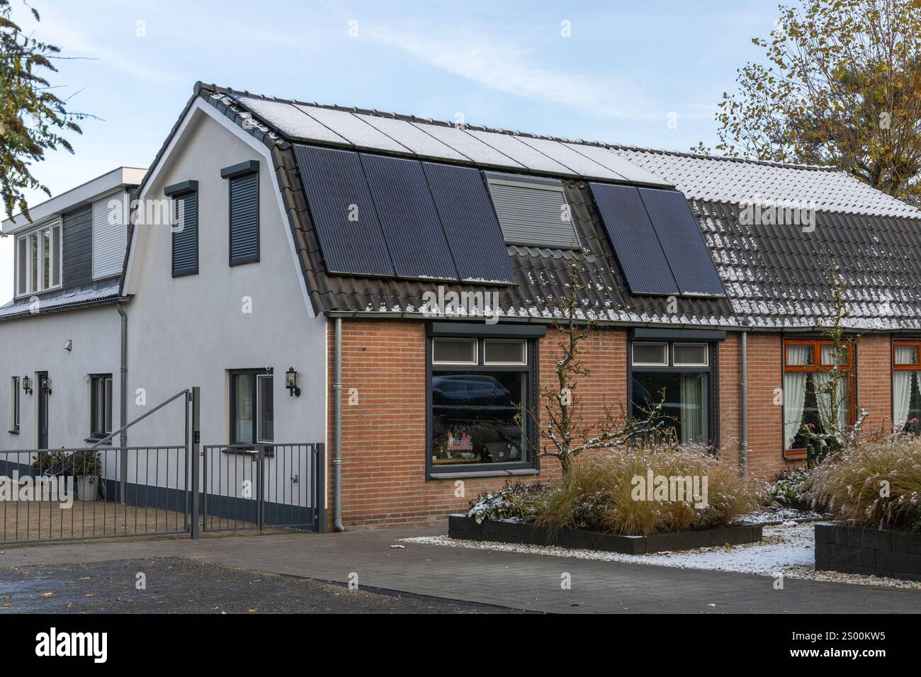 Leerdam, Niederlande. 21. November 2024. Private Solarpaneele mit Schnee und eine Hälfte ohne Schnee auf einem Familienhaus auf dem Dach im Winter. Stockfoto