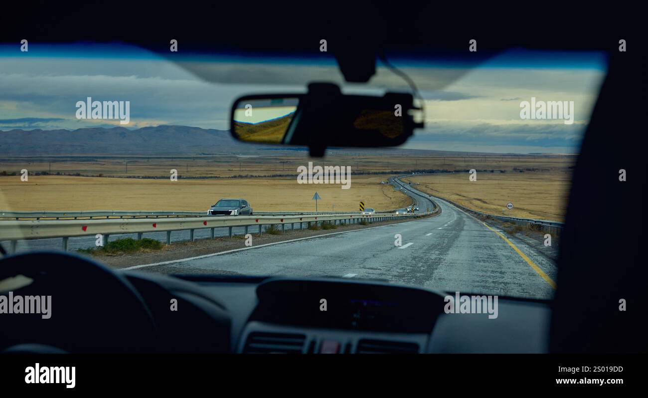 Blick durch die Frontscheibe der Autofahrt bei Regenwetter auf der Bergstraße mit Lkws. Fahren Sie weit weg, Fahrer mit Lenkradsilhouette po Stockfoto