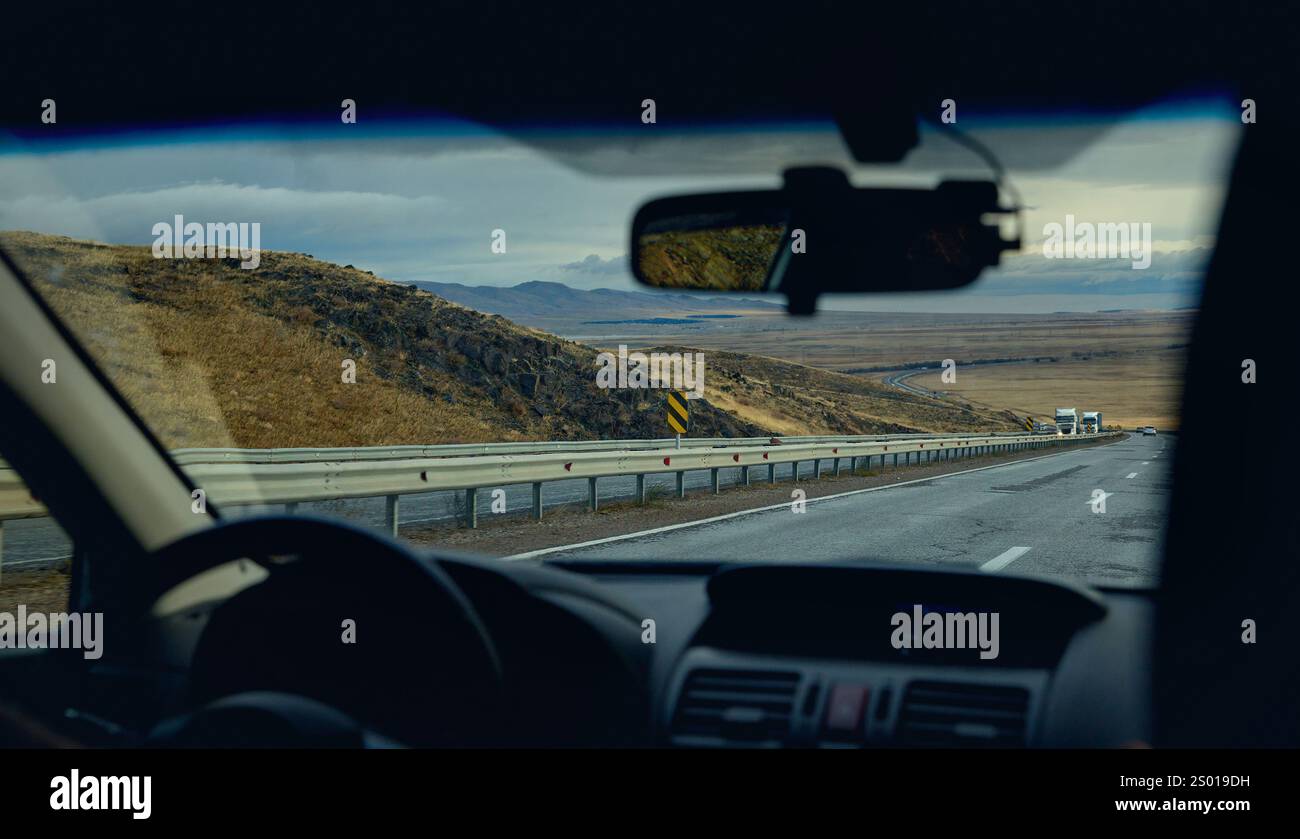 Blick durch die Frontscheibe der Autofahrt bei Regenwetter auf der Bergstraße mit Lkws. Fahren Sie weit weg, Fahrer mit Lenkradsilhouette po Stockfoto