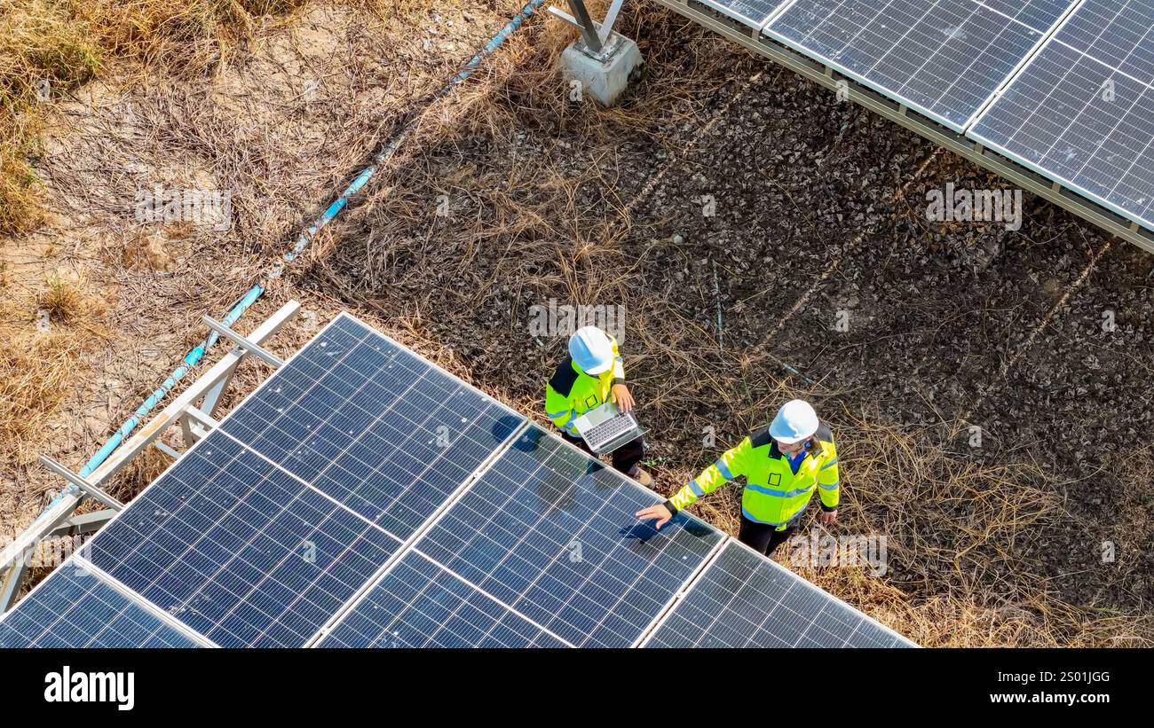 Zwei Arbeiter mit Schutzhüten und reflektierenden Westen untersuchen Solarpaneele in einem Solarpark genau. Sie sind mit Instandhaltungsaufgaben unter c Stockfoto