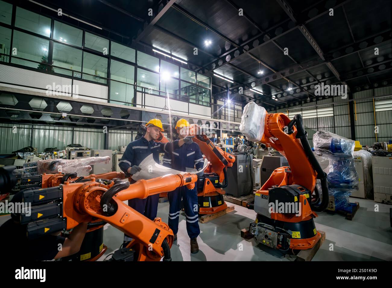 Zwei Ingenieure diskutieren Pläne, während sie Roboterarme in einem High-Tech-Fertigungswerk betreiben und fortschrittliche Automatisierungstechnik vorführen Stockfoto