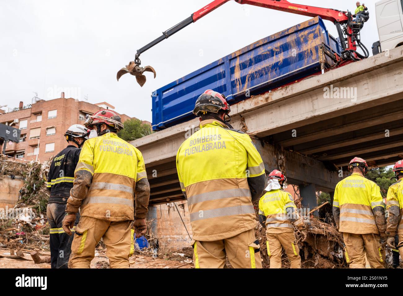 DANA-Flutungseffekte. Überschwemmungseinflüsse, Valencia, Spanien. Feuerwehrleute auf der Suche nach vermissten Personen im Flussbett und Bagger für Materialumschlag Stockfoto