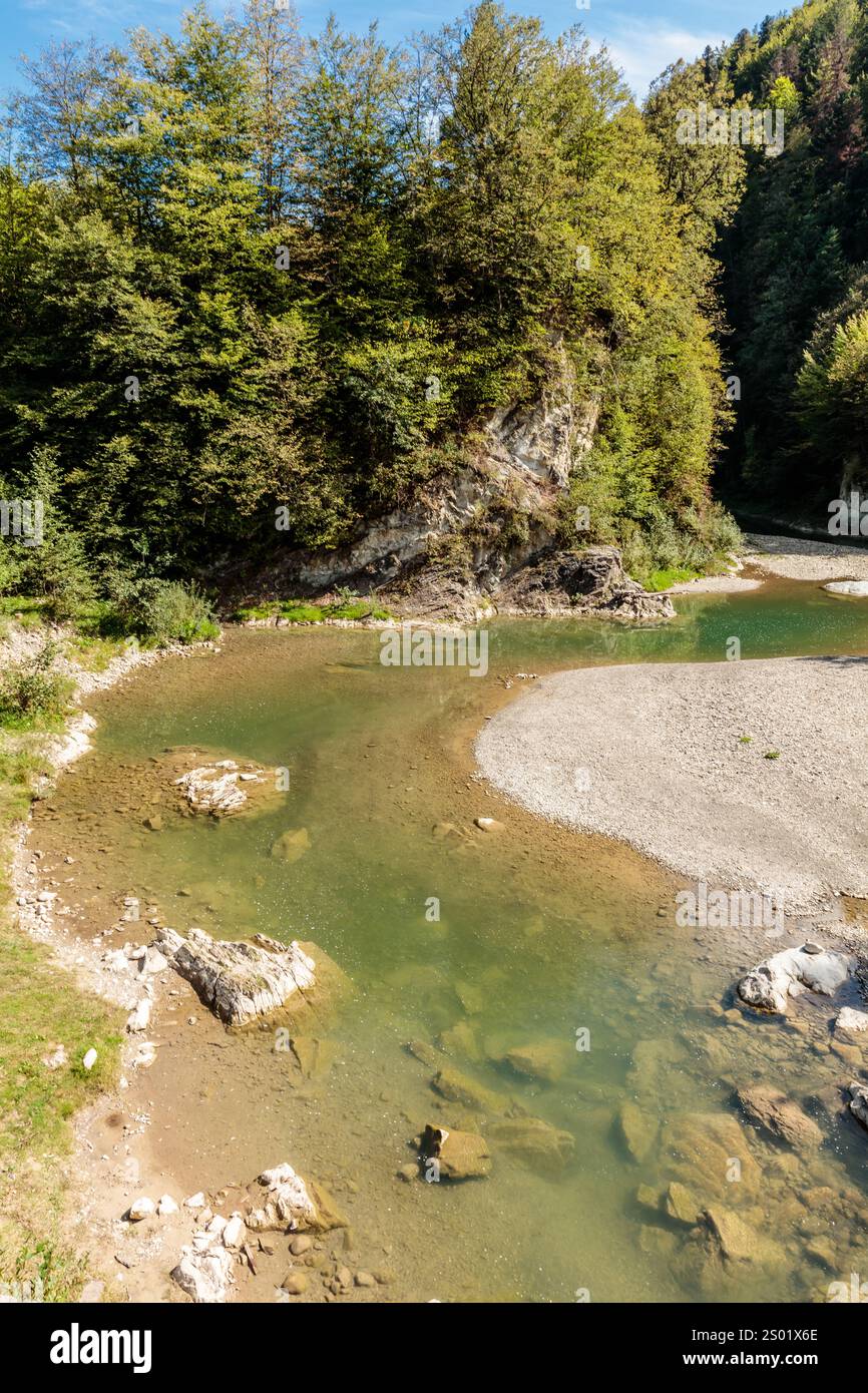 Ein Fluss mit einer felsigen Küste und Bäumen im Hintergrund. Das Wasser ist klar und ruhig Stockfoto