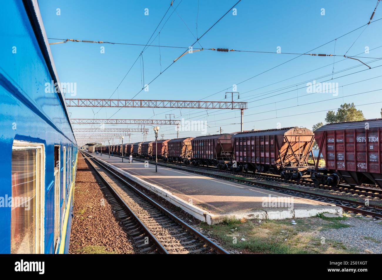 Ein Zug sitzt auf den Gleisen mit einem blauen Zugwagen im Vordergrund. Der Zug ist von vielen Güterwagen umgeben und der Himmel ist klar und blau Stockfoto
