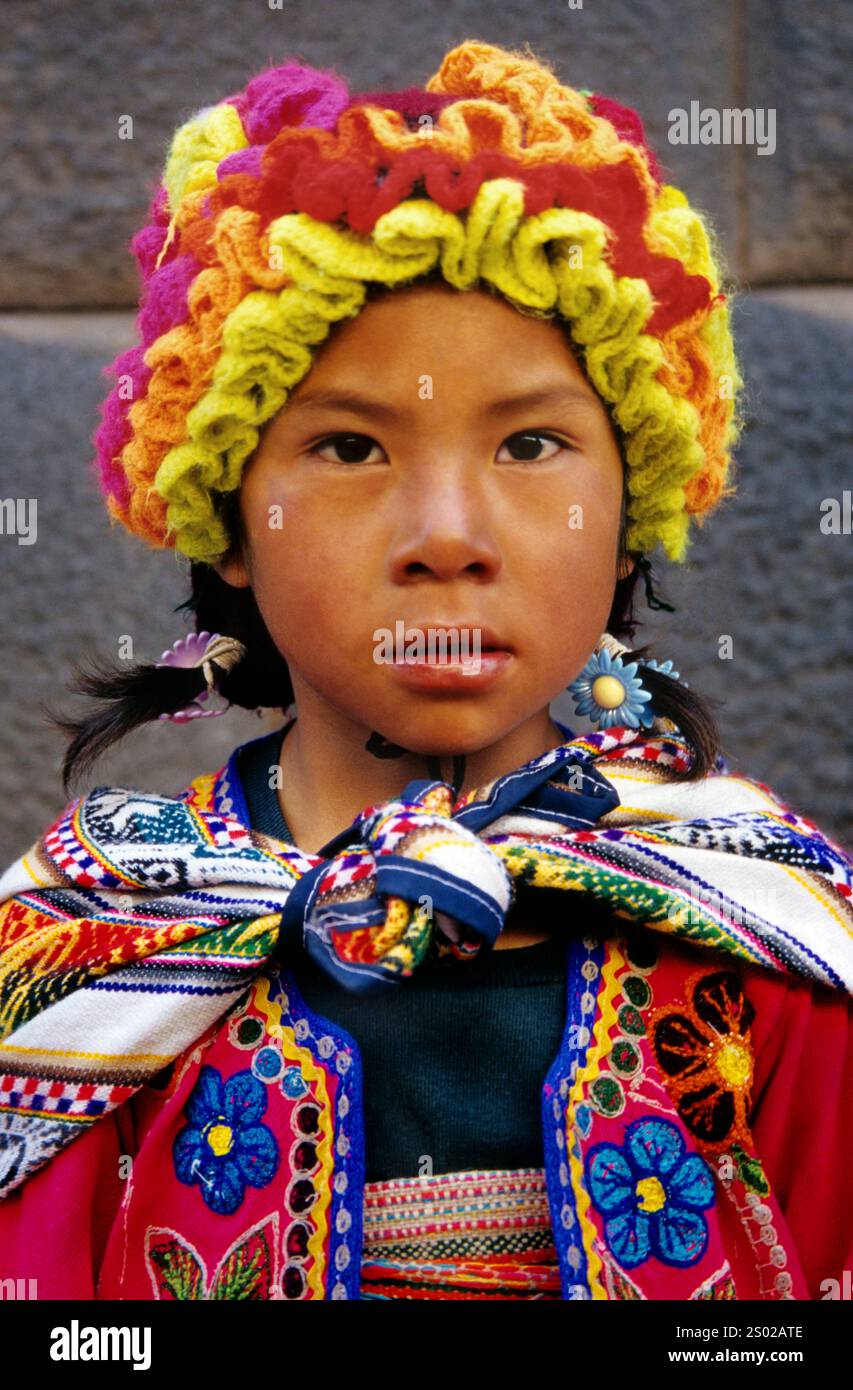 Indigenes Mädchen in traditioneller Quechua-Kleidung in Cusco, Peru, trägt lebendige handgefertigte Textilien und einen farbenfrohen Kopfschmuck, der die Andenkultur widerspiegelt. Stockfoto
