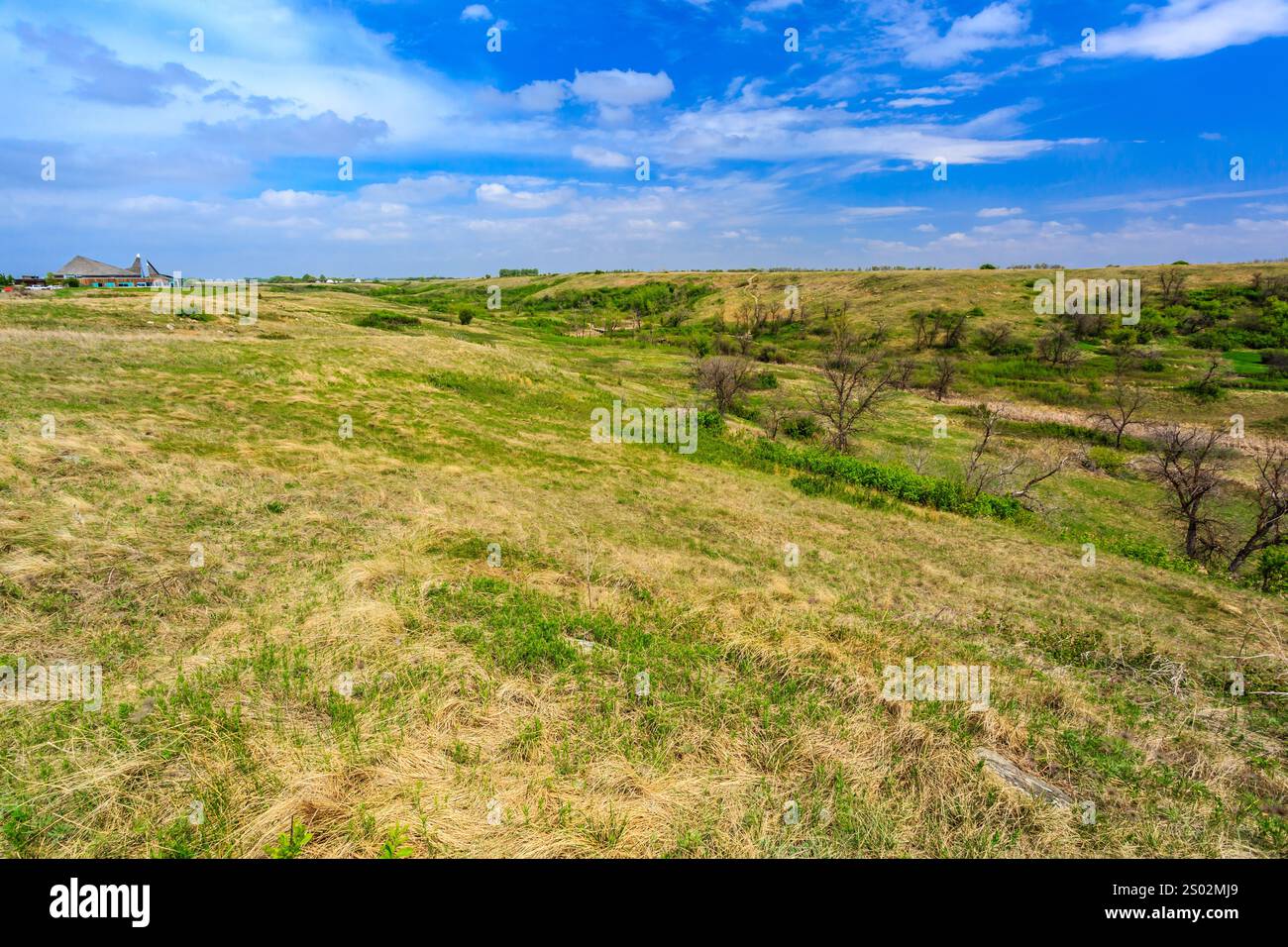 Ein großes, leeres Feld mit einem Haus in der Ferne. Der Himmel ist blau und es gibt ein paar Wolken Stockfoto
