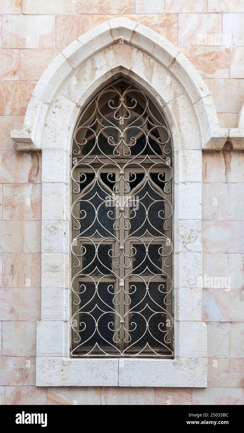 Ein wunderschön gefertigtes gotisches Fenster ziert eine alte Steinmauer mit künstlerischen Metallarbeiten. Stockfoto