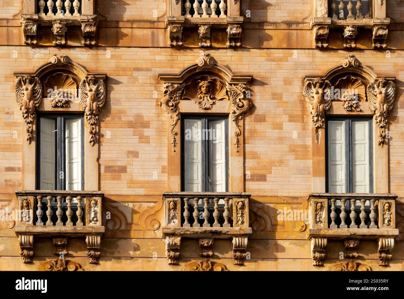 Nahaufnahme einer historischen Gebäudefassade mit verzierten Balkonen und dekorativen Elementen um die Fenster. Stockfoto