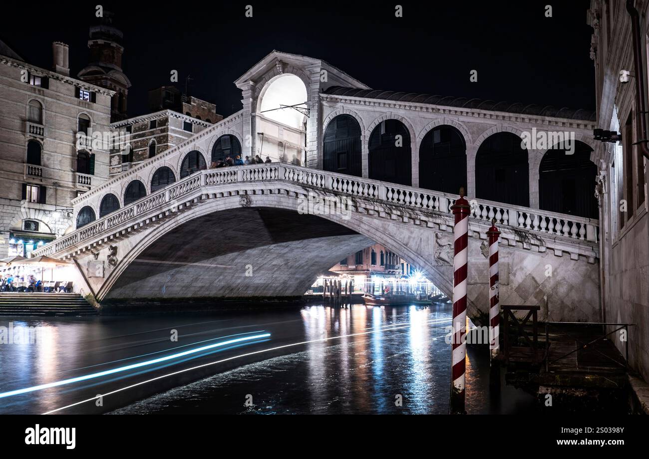 Ein atemberaubender Blick bei Nacht auf die Rialto-Brücke in Venedig, beleuchtet vor dem dunklen Himmel. Die Brücke verfügt über elegante Bögen und komplizierte Details, mit Stockfoto