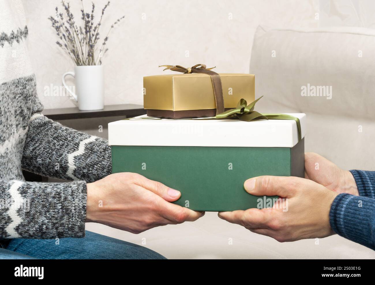 Zwei Personen tauschen wunderschön verpackte Geschenke in einem stilvollen Wohnzimmer mit Wärme und Weihnachtsstimmung aus. Stockfoto