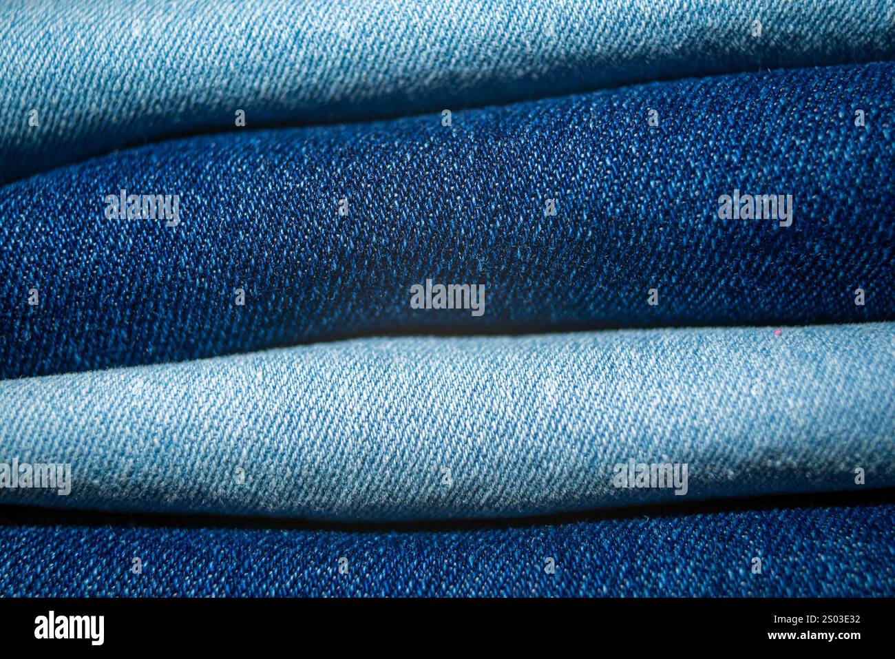 Nahaufnahme des gefalteten Jeansmaterials mit kräftigen Texturen und verschiedenen Blautönen, die die Qualität und den Stil des Materials hervorheben. Stockfoto