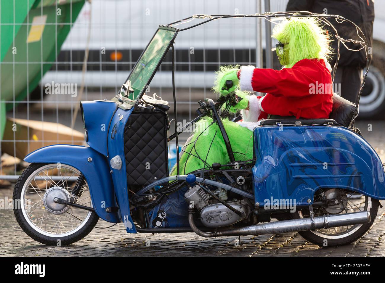 Erfurt, Deutschland. Dezember 2024. Ein Reiter, der als Grinch gekleidet ist, steht auf dem Domplatz mit seinem „Duo“-Moped. Die traditionelle Fahrt, bei der Mopedfahrer, die sich zu Weihnachten verkleidet haben, zu einer Tour durch die Hauptstadt des Bundesstaates treffen, wurde dieses Jahr aufgrund der Gefahr vereister Straßen kurzfristig abgesagt. Quelle: Michael Reichel/dpa/Alamy Live News Stockfoto