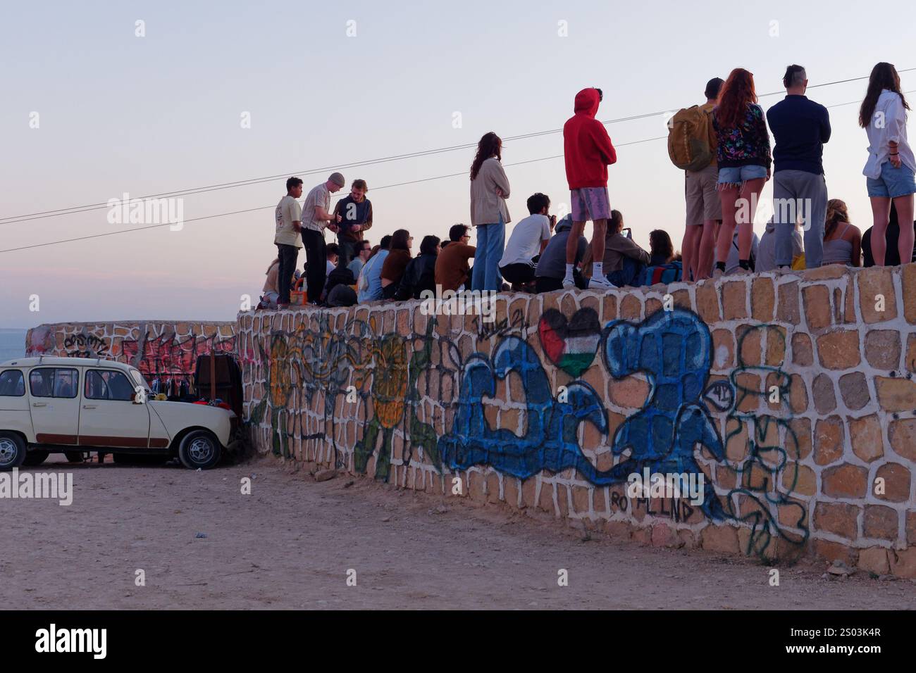 Die Zuschauer in einem Skate Park stehen auf einer Graffiti-Wand mit einem Retro-Auto im Dorf Taghazout, Marokko. Dezember 2024 Stockfoto