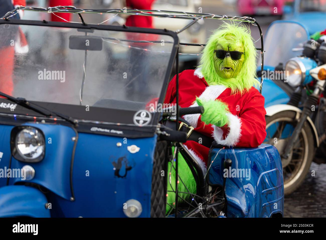 Erfurt, Deutschland. Dezember 2024. Ein Reiter, der als Grinch gekleidet ist, steht auf dem Domplatz mit seinem „Duo“-Moped. Die traditionelle Fahrt, bei der Mopedfahrer, die sich zu Weihnachten verkleidet haben, zu einer Tour durch die Hauptstadt des Bundesstaates treffen, wurde dieses Jahr aufgrund der Gefahr vereister Straßen kurzfristig abgesagt. Quelle: Michael Reichel/dpa/Alamy Live News Stockfoto