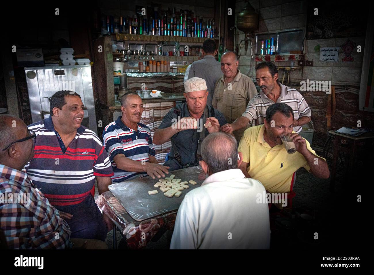 Ein lebhaftes Treffen ägyptischer Männer, die Dominospiele spielen und Tee in einem traditionellen Café in Alexandria, Ägypten, genießen. Die Szene spiegelt Kameradschaft wider Stockfoto