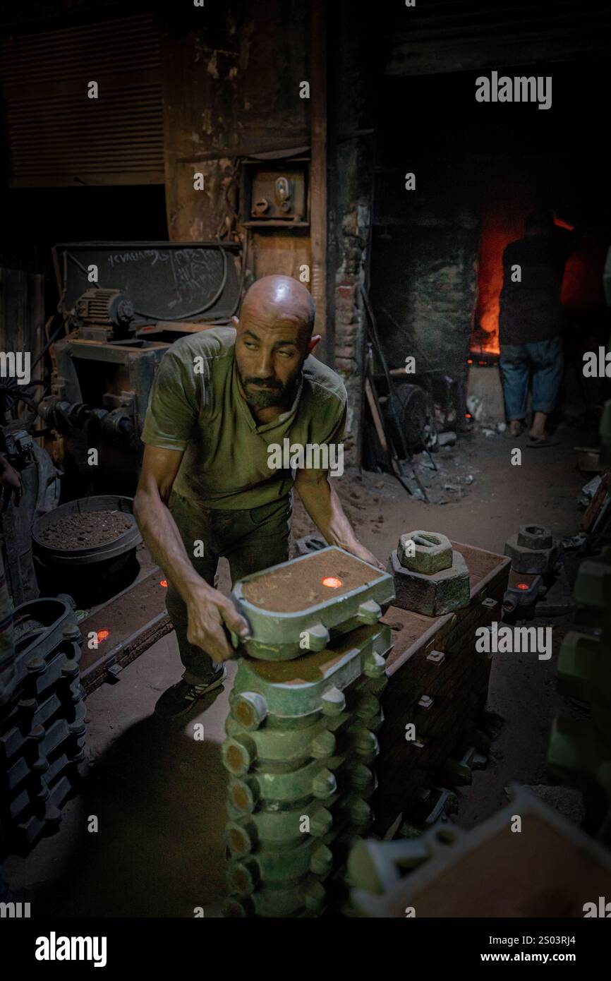 Ein Gießereiarbeiter, der eine Form in einer Metallwerkstatt in Alexandria, Ägypten, akribisch bearbeitet. Die Szene zeigt traditionelle Handwerkskunst . Stockfoto
