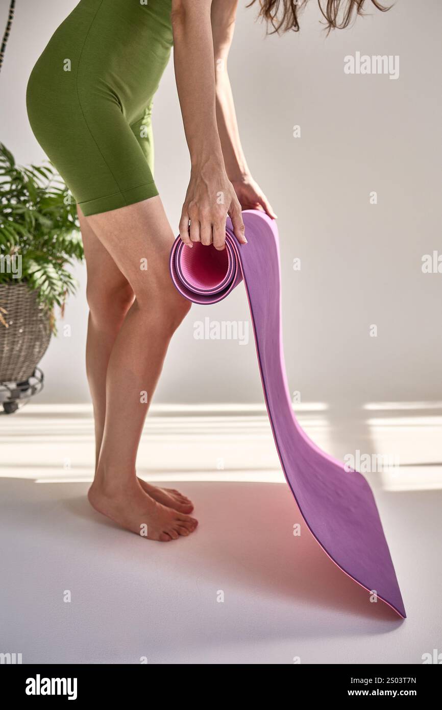 Lady in grünen Shorts rosa Yogamatte ausrollen, sich auf Training vorbereiten, Fitness-Aktivität, Indoor-Workout, gesundes Lifestyle-Konzept Stockfoto