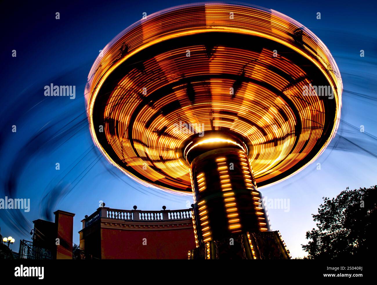Eine lebhafte Karussellfahrt mit hellen Lichtern, die in Bewegung vor dem Himmel der Dämmerung aufgenommen werden. Die Drehbewegung erzeugt ein dynamisches und festliches A Stockfoto