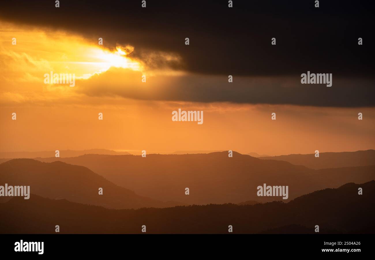 Helle Sonnenstrahlen das Licht scheint bei Sonnenuntergang durch dunkle Wolken über dem Berg. Dramatischer Himmel im Winter. Horizont über Land Stockfoto