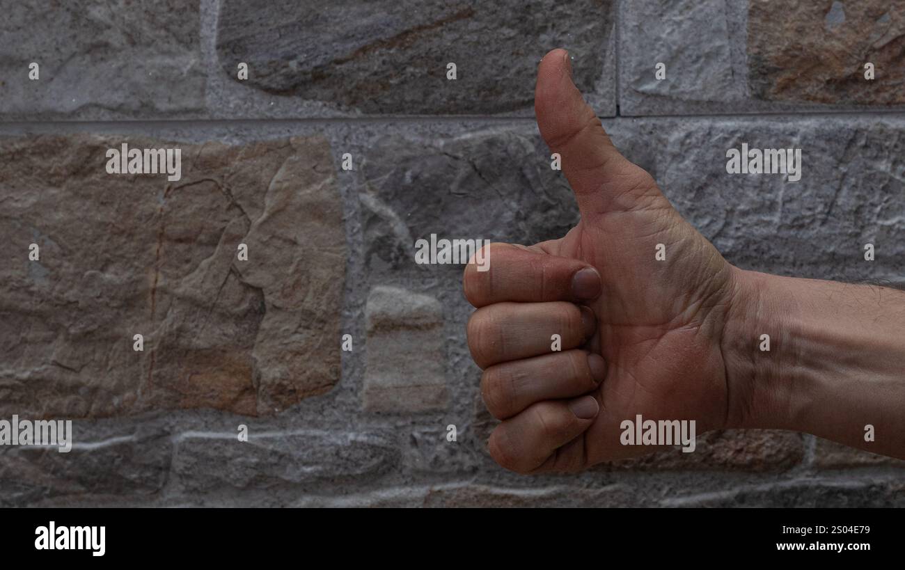 Nahaufnahme einer menschlichen Hand, die einen Daumen gegen eine abwechslungsreiche Steinmauer zeigt, die Anerkennung mit einem strukturierten Hintergrund symbolisiert Stockfoto