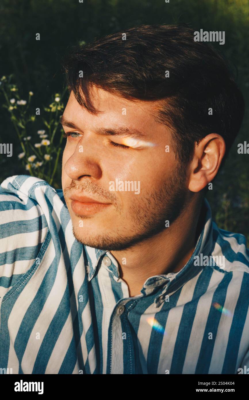 Ein detailliertes Porträt eines Mannes mit dunklen Haaren und gestreiftem Hemd, hervorgehoben durch eine Kulisse aus weißen Gänseblümchen. Die lebendigen Blumen bringen Harmonie und nat Stockfoto