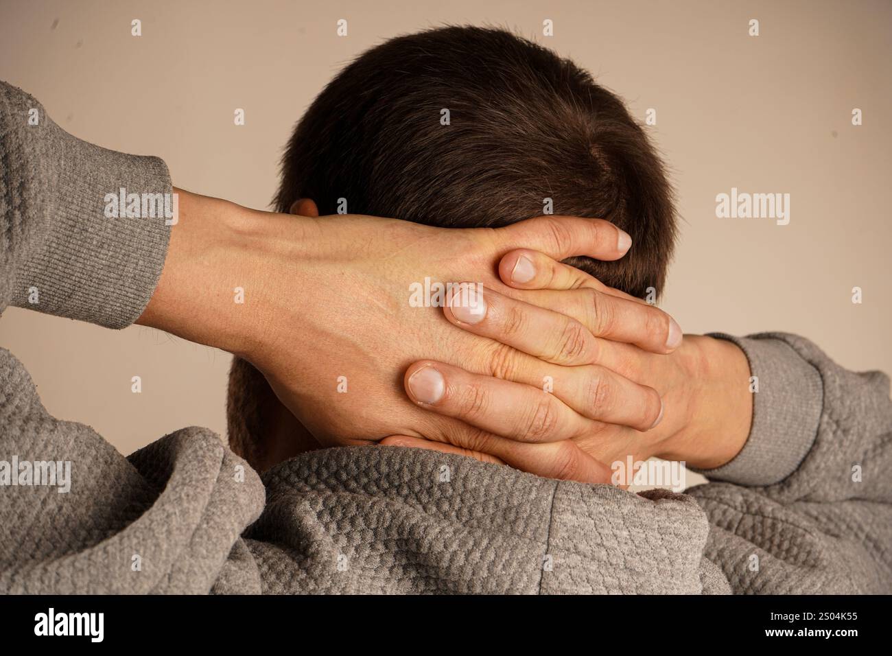 Nahaufnahme von gefalteten Händen auf dem Hinterkopf eines Mannes. Das minimalistische Ambiente betont die symbolische Bedeutung der Einheit und des Zusammenspiels der Geste Stockfoto