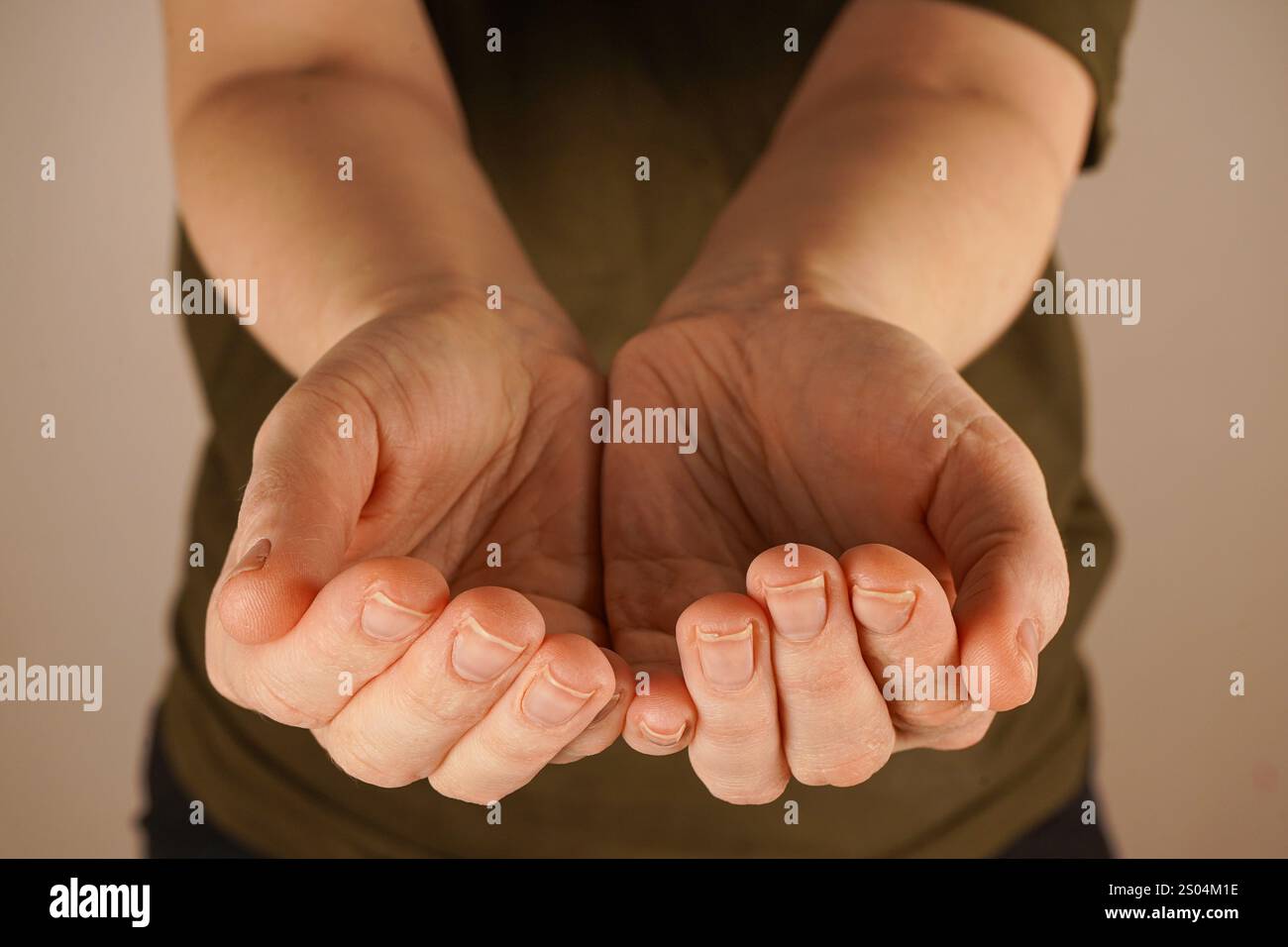 Der minimalistische Hintergrund vor einer hellen Wand verstärkt die emotionale Tiefe dieser sanften, durchdachten Geste. Zwei Handflächen sind umschlossen Stockfoto
