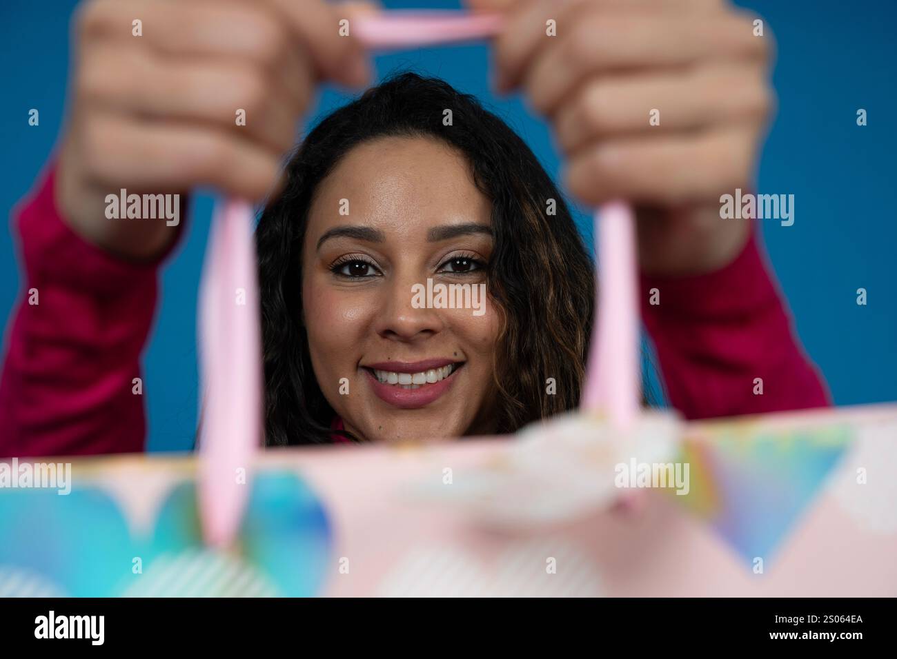 Junge Frau, die eine Geschenktüte mit rosafarbenen Griffen auf blauem Hintergrund zeigt Stockfoto