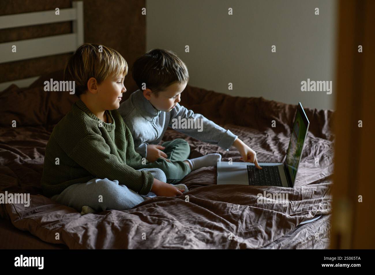 Kinder sitzen vor dem Laptop auf dem Bett, um adaptives Lernen zu ermöglichen Stockfoto
