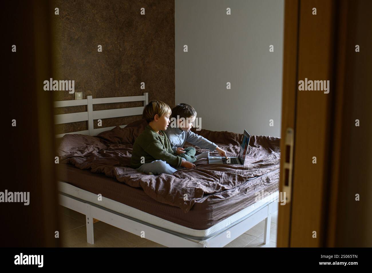 Kinder sitzen vor dem Laptop auf dem Bett, um adaptives Lernen zu ermöglichen Stockfoto