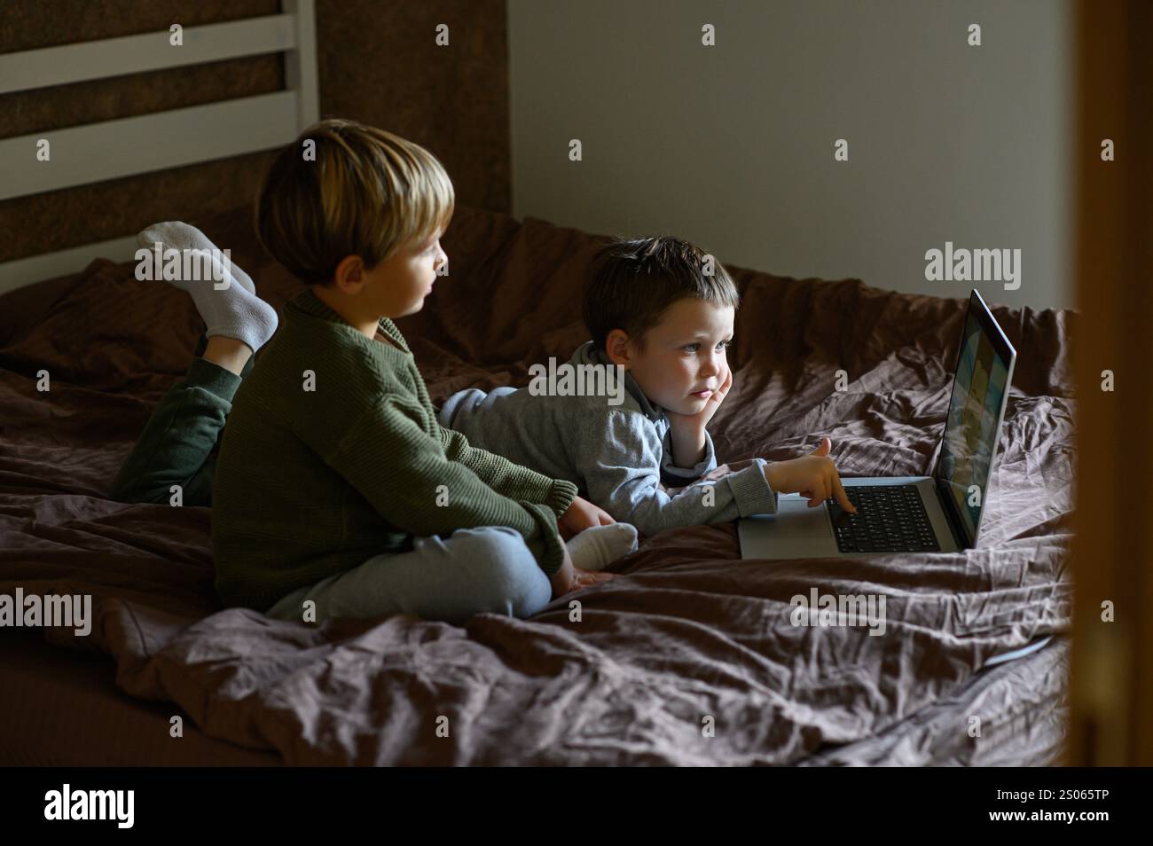 Kinder sitzen vor dem Laptop auf dem Bett, um adaptives Lernen zu ermöglichen Stockfoto
