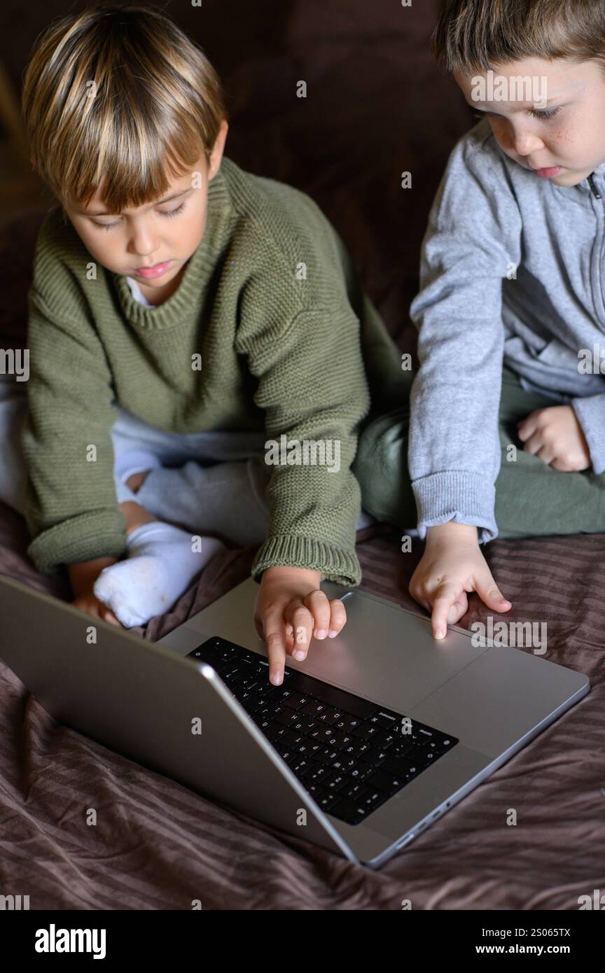 Kinder sitzen vor dem Laptop auf dem Bett, um adaptives Lernen zu ermöglichen Stockfoto