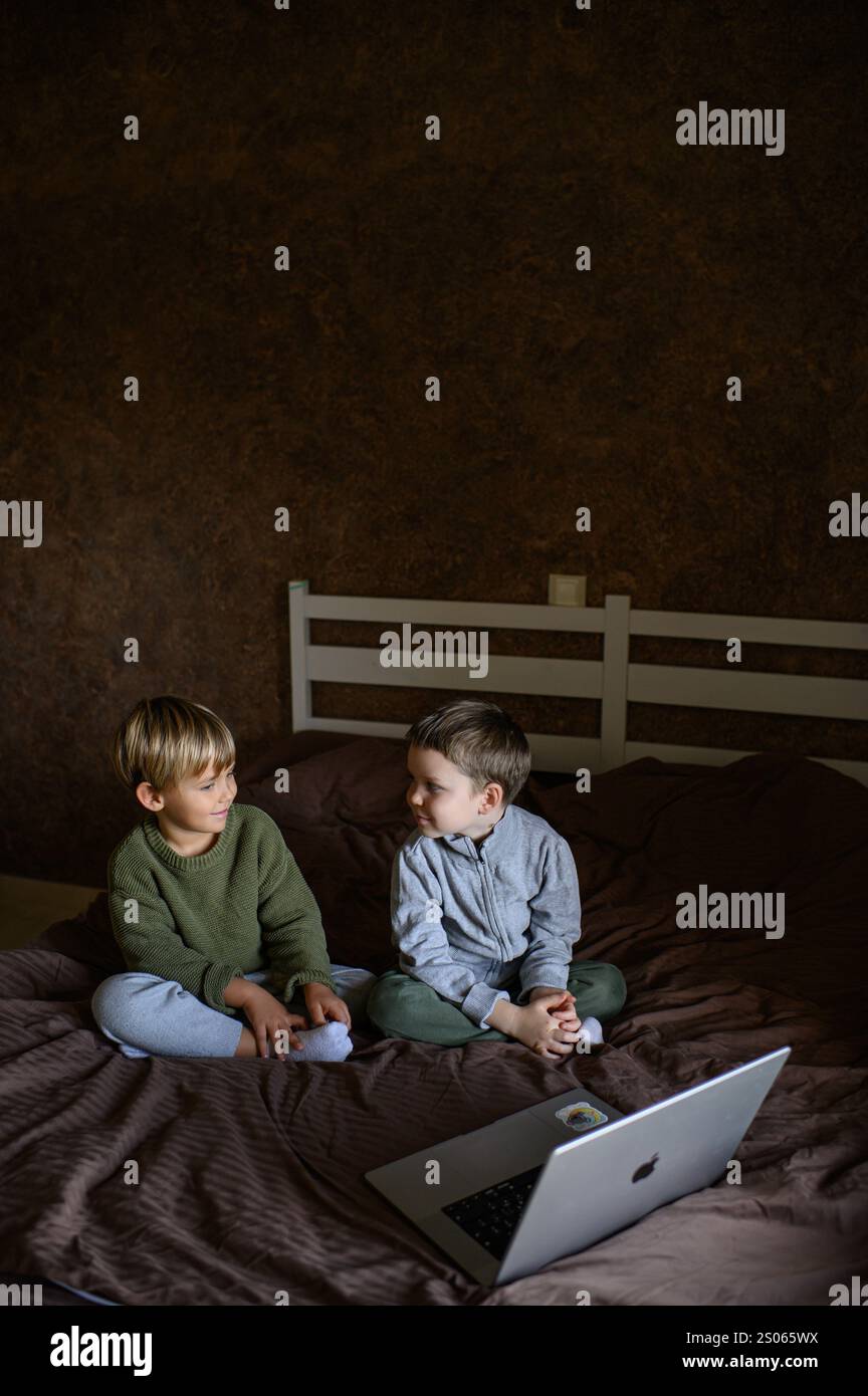 Kinder sitzen vor dem Laptop auf dem Bett, um adaptives Lernen zu ermöglichen Stockfoto